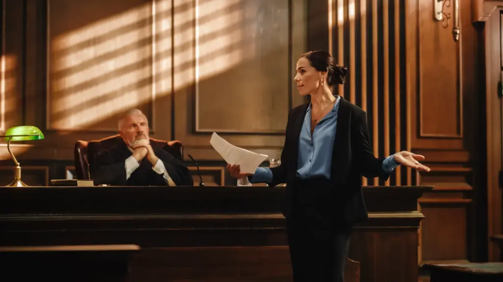 An attorney speaking to the courtroom with a judge behind her.
